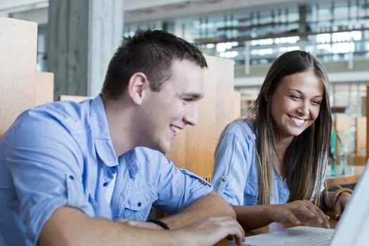 Two people siting on front of a Laptop, happily working on it
